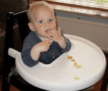 Een baby eet zelf wat hapjes in zijn stoeltje.