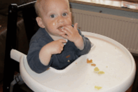 Een baby eet zelf wat hapjes in zijn stoeltje.