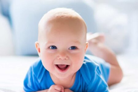 Een baby op de buik, vrolijk kijkend.