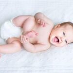 Een baby ligt lachend met voetje te spelen.