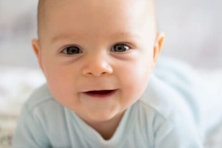 Baby kijkt lachend in de camera.